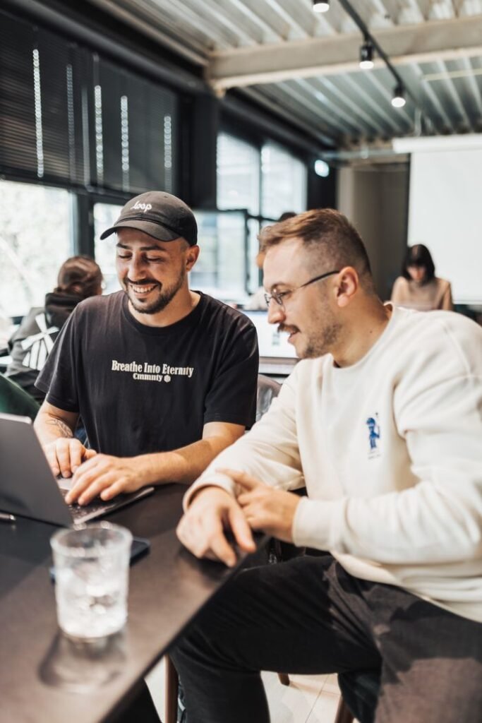 pexels-photo-18999184-18999184 Two young men smiling and collaborating on a laptop in a modern office atmosphere.